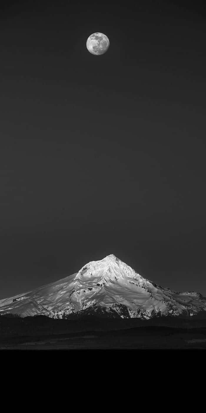 A Black And White Photo Of A Mountain With A Moon In The Sky
