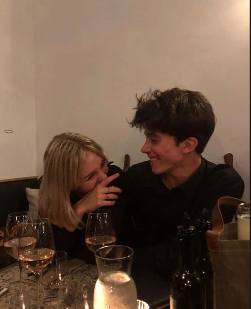 A Man And Woman Are Sitting At A Table With Wine Glasses