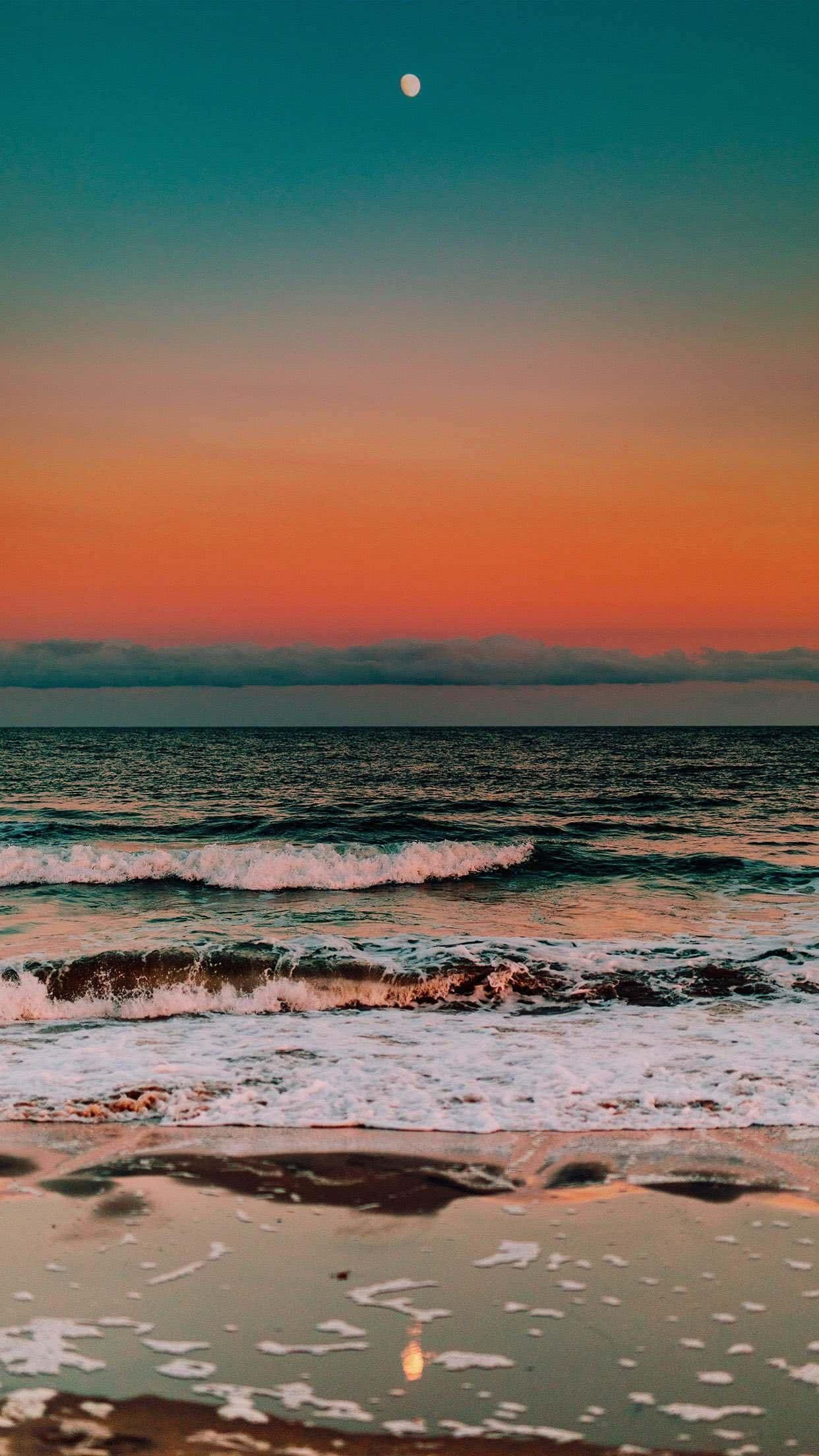 A Sunset On The Beach With The Moon Reflecting In The Water