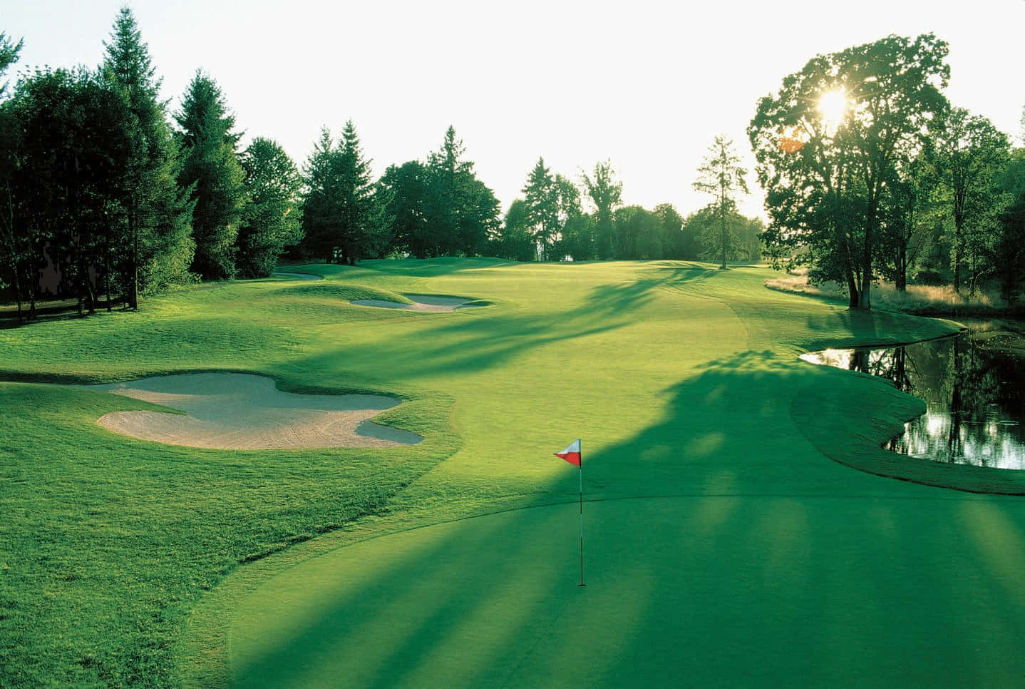 A Golf Course With A Pond And Trees Wallpaper