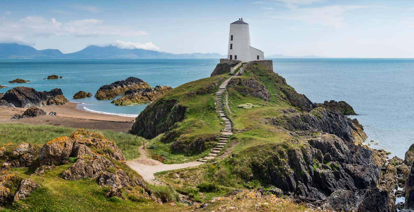 A Lighthouse Sits On Top Of A Rocky Cliff Wallpaper