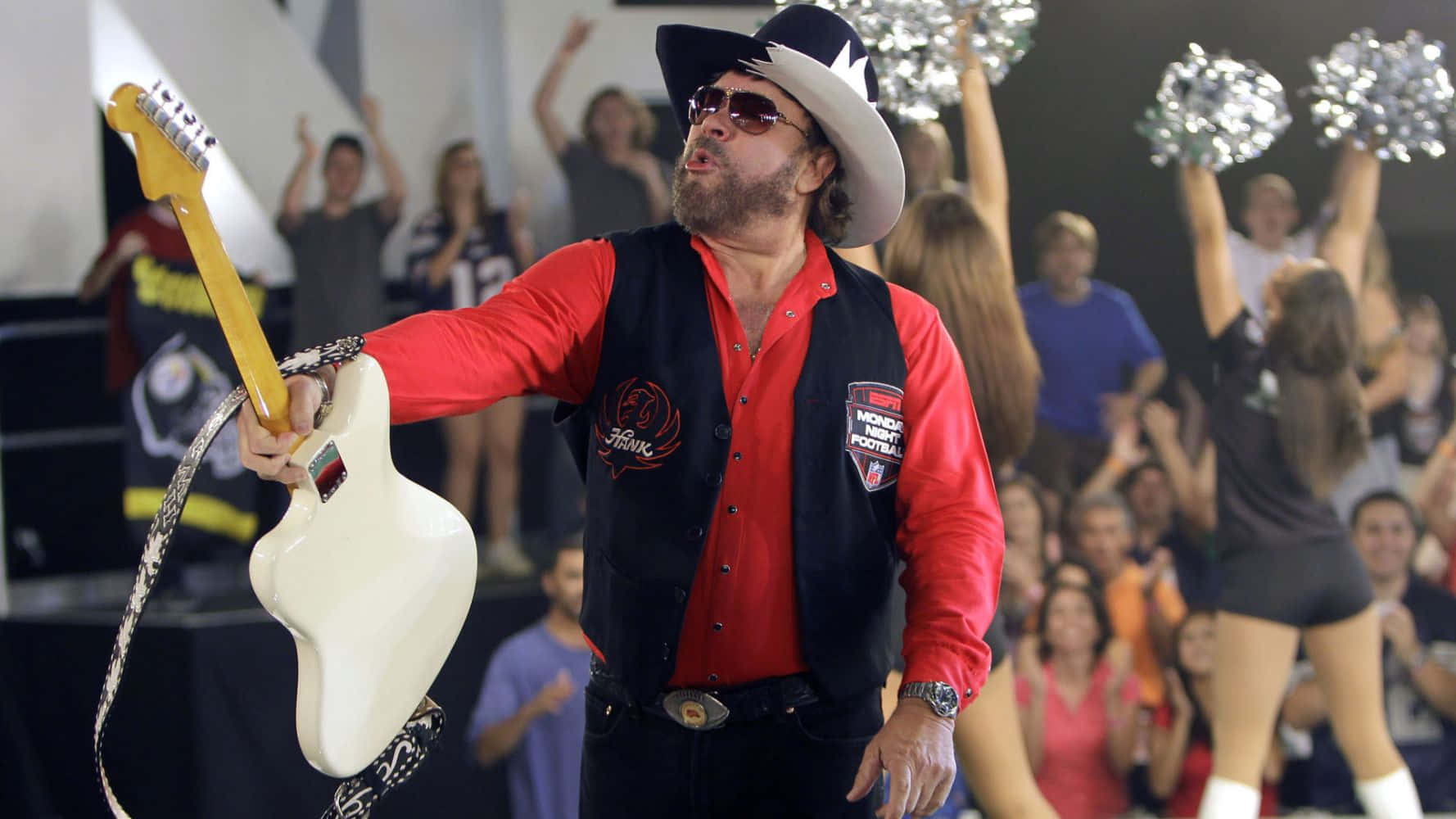 A Man In A Hat And Red Vest Holding A Guitar Wallpaper