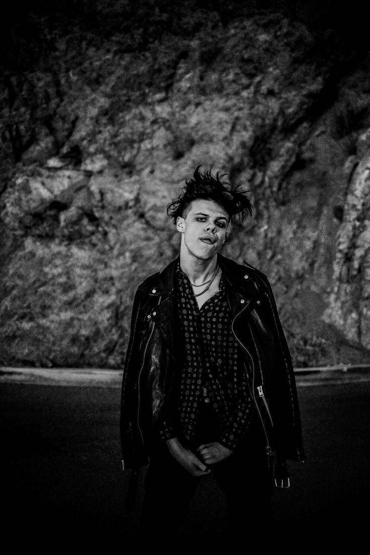 A Man In A Leather Jacket Standing In Front Of A Rock Wallpaper