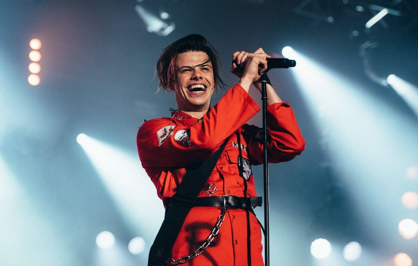 A Man In Red Is Singing Into A Microphone Wallpaper