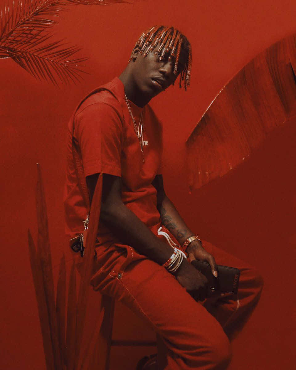 A Man In Red Sitting On A Chair With Palm Trees Behind Him Wallpaper