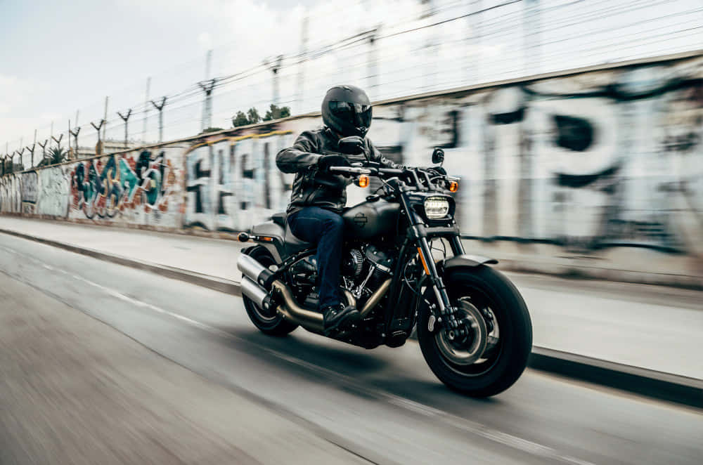 A Man Riding A Motorcycle On A Street With Graffiti Wallpaper