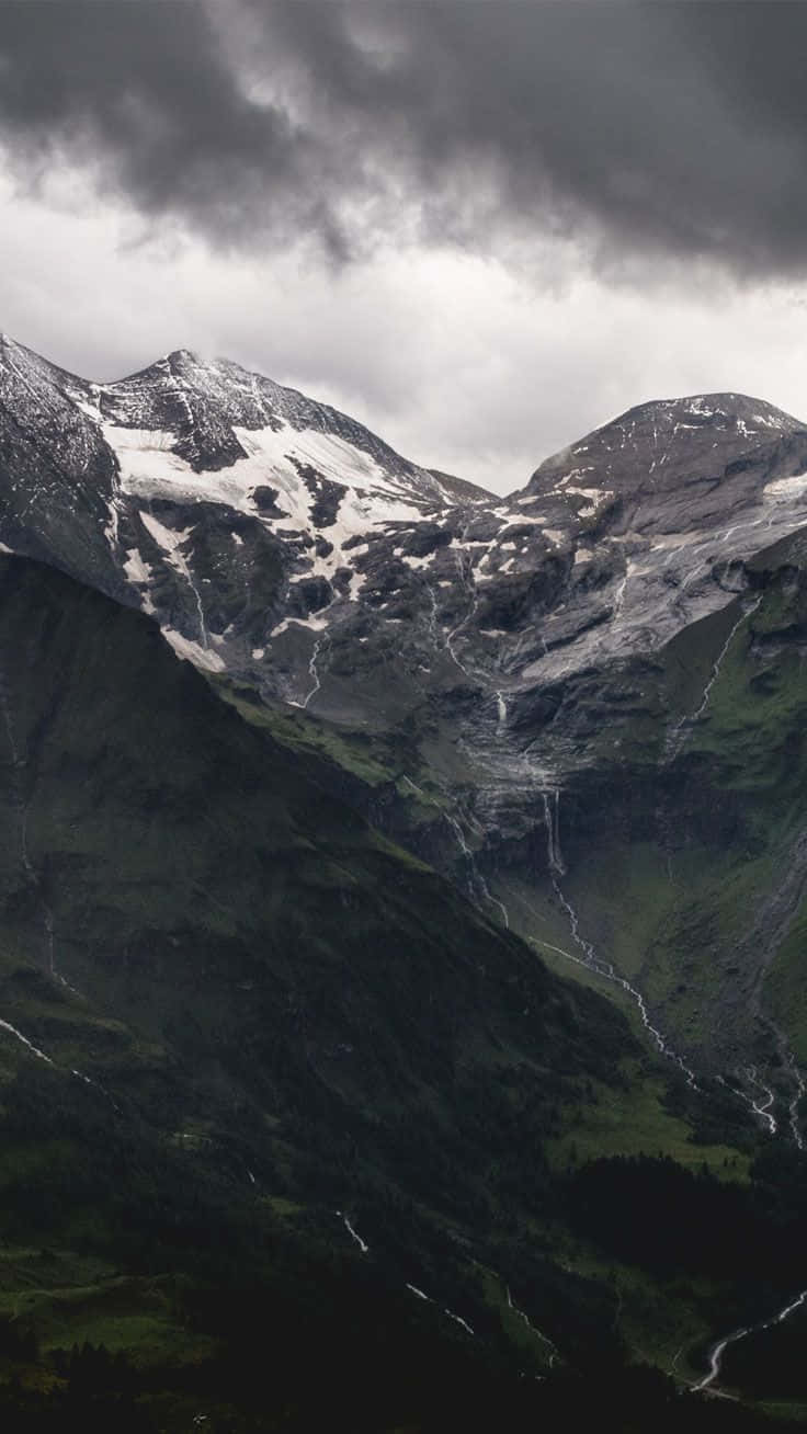 A Mountain Range With Snow Covered Mountains Under A Cloudy Sky Wallpaper