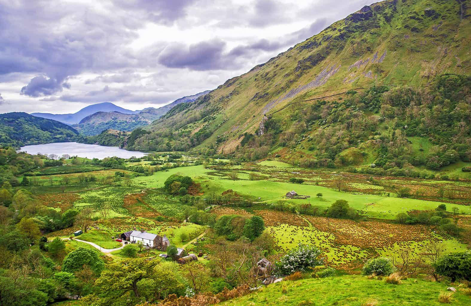 A View Of A Valley With A Lake And Green Grass Wallpaper