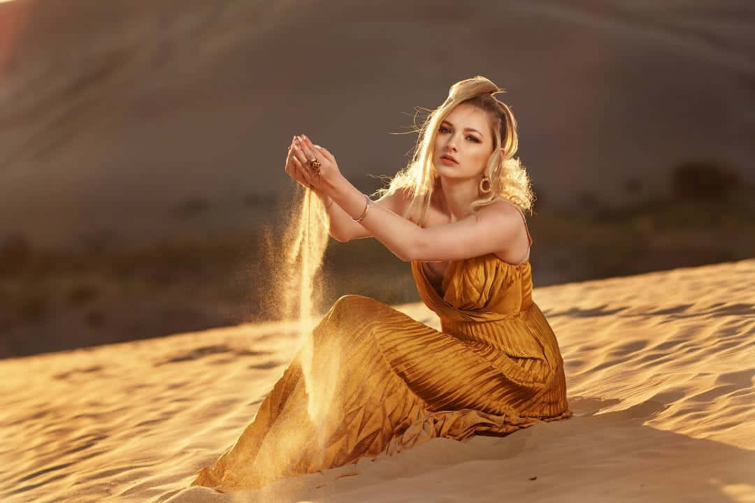 A Woman In A Yellow Dress Is Sitting On A Sand Dune Wallpaper