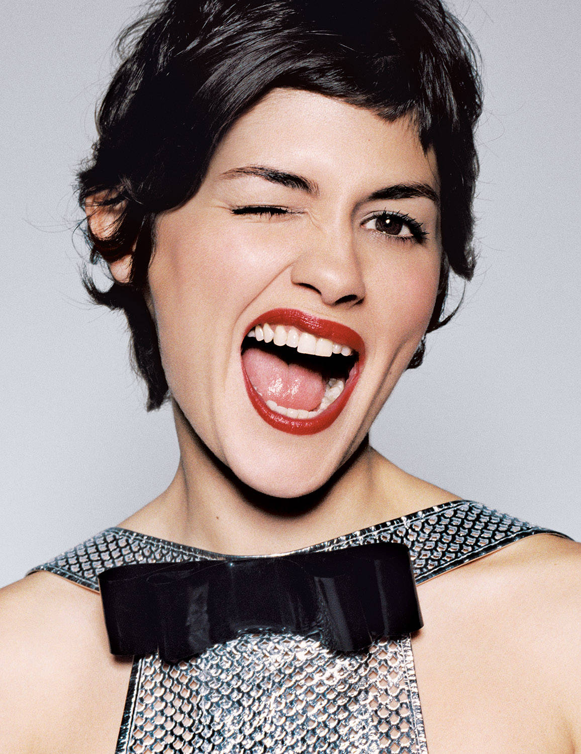 Audrey Tautou Winking In Elegant Silver Dress Wallpaper