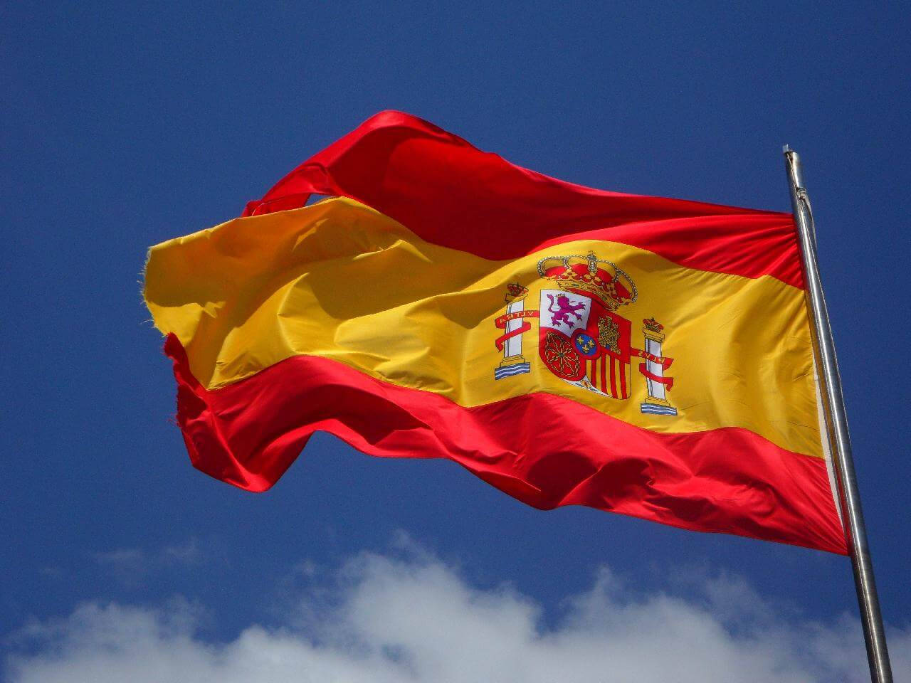 Caption: Spain's National Pride - Magnificent Spain Flag Soaring High Against The Clear Blue Sky Wallpaper
