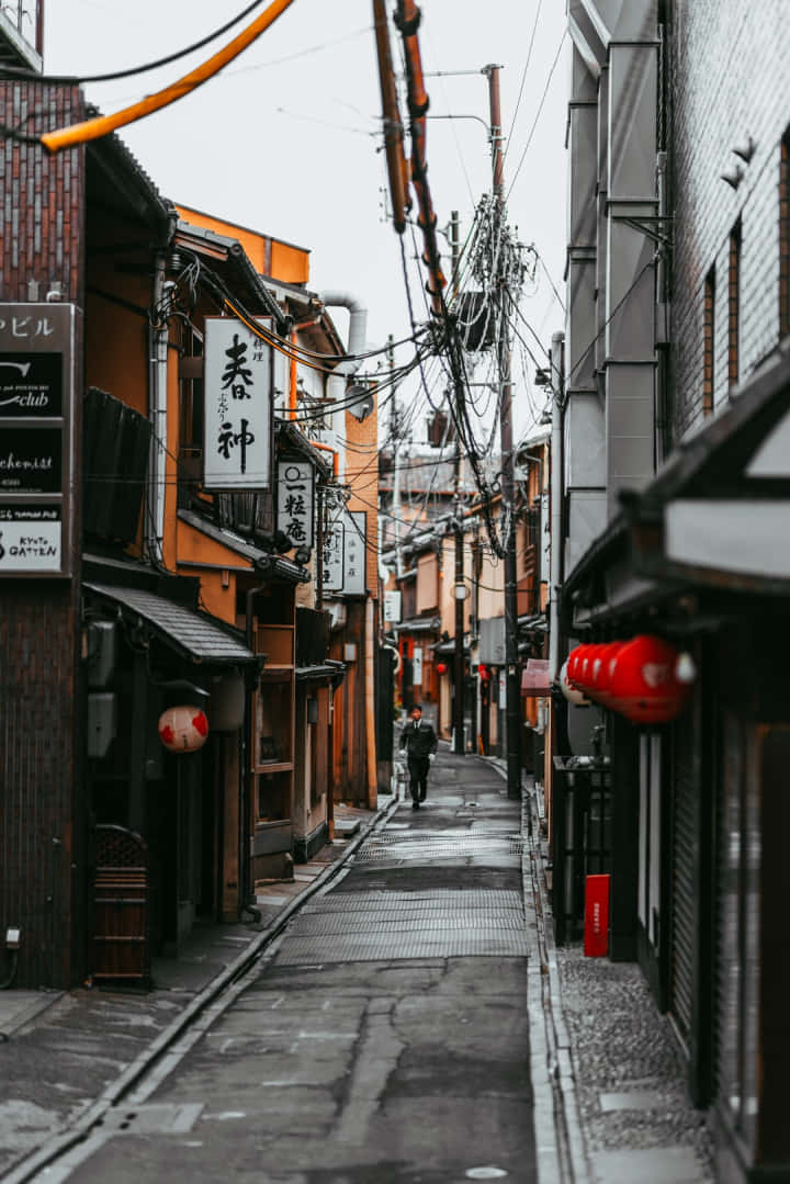 Charming Exploration - A Solitary Wanderer Traverses A Narrow Street In Japan. Wallpaper