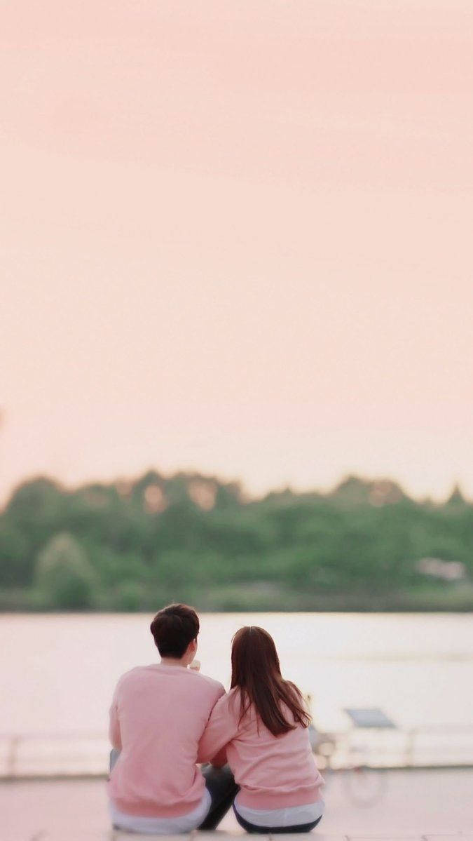 Cute Couple In Pink Shirts Viewing River Wallpaper