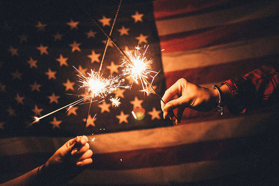 Dark American Flag Behind Two Hands Holding Sparklers Wallpaper