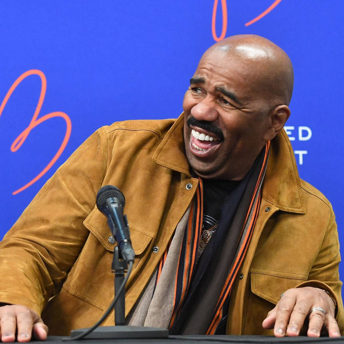 Enthusiastic Steve Harvey Holding A Microphone And Laughing Wallpaper