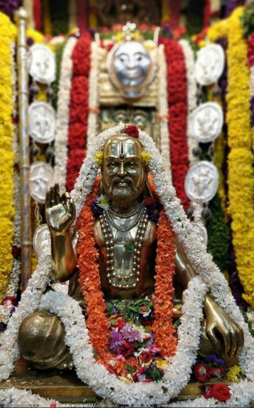 Majestic Golden Statue Of Raghavendra Adorned With Floral Garlands Wallpaper