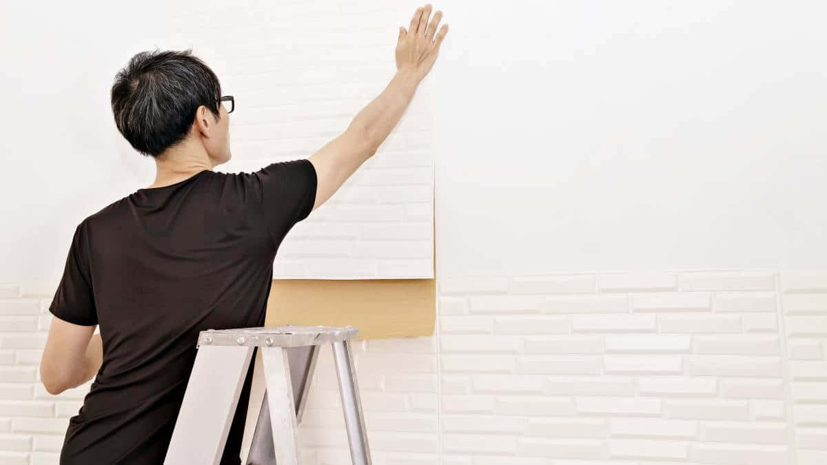 Man Applying Wallpaper Standingon Ladder Wallpaper