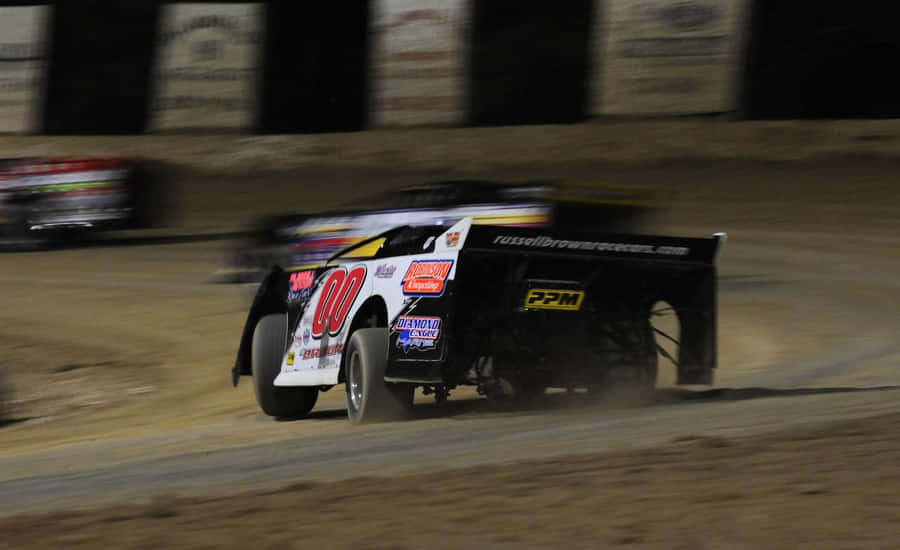 A Dirt Track With Several Cars Racing At Night Wallpaper
