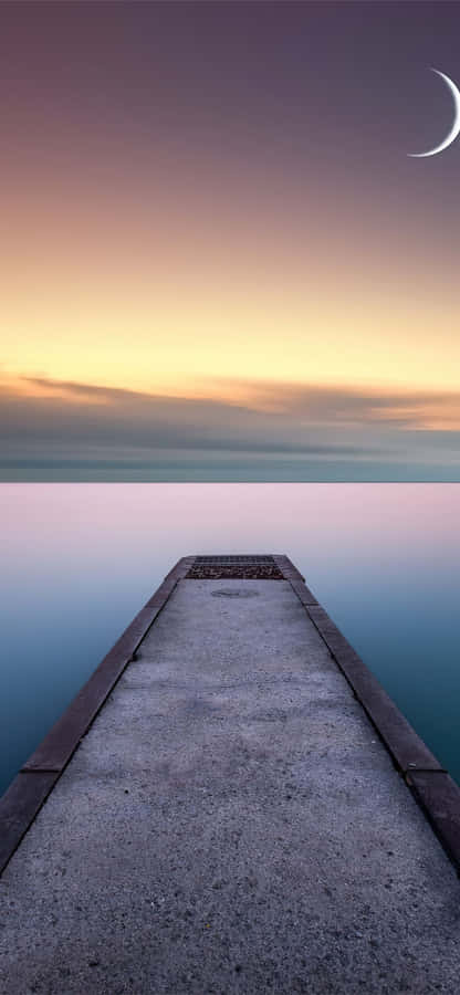 A Pier Leading To The Water With A Crescent Moon Wallpaper