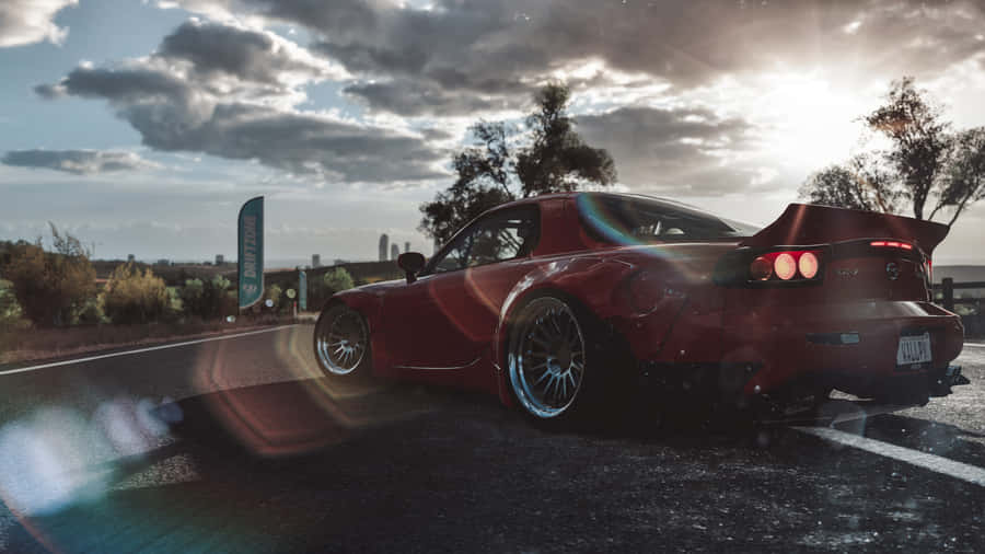 A Red Car Is Parked On A Road With A Sun Behind It Wallpaper
