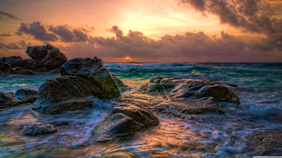 A Sunset Over The Ocean With Rocks And Water Wallpaper