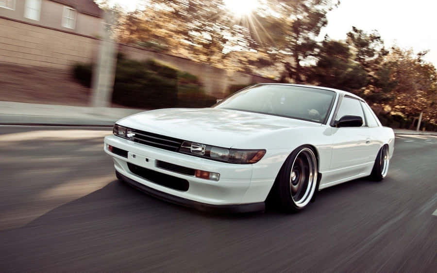 A White Car Driving Down The Street Wallpaper