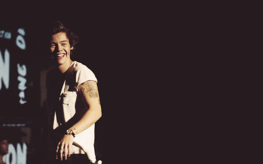 Harry Styles Looking Content As He Types On His Laptop Wallpaper