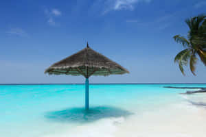 A Beach With A Thatched Umbrella Wallpaper