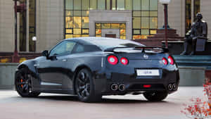A Black Sports Car Parked In Front Of A Statue Wallpaper