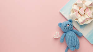 A Blue Crochet Cat With Marshmallows On A Pink Background Wallpaper