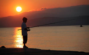 A Boy's Peaceful Moment Of Fishing At Sunset Wallpaper