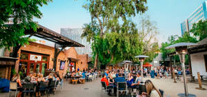 A Crowd Of People Sitting At Tables In A Courtyard Wallpaper