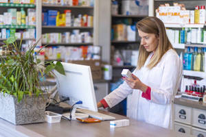 A Diligent Female Pharmacist Perusing Medication In A Pharmacy Wallpaper