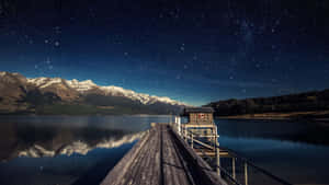 A Dock With A Starry Sky And Mountains Wallpaper