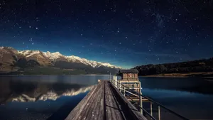 A Dock With A Starry Sky And Mountains Wallpaper