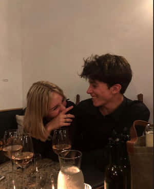 A Man And Woman Are Sitting At A Table With Wine Glasses Wallpaper