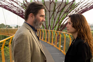 A Man And Woman Standing Next To Each Other On A Bridge Wallpaper