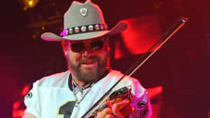 A Man In A Cowboy Hat And Sunglasses Playing A Guitar Wallpaper