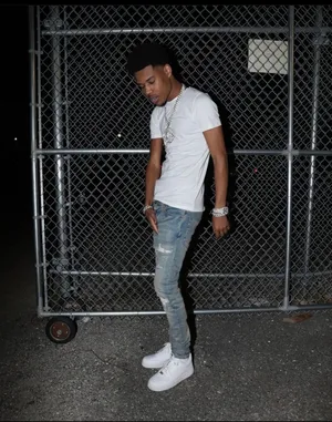 A Man In A White Shirt And Jeans Standing In Front Of A Fence Wallpaper