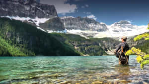 A Man Standing In The Water Near A Mountain Wallpaper