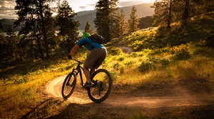 A Mountain Biker Racing Downhill Against The Backdrop Of A Breath-taking Sunset. Wallpaper