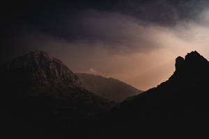 A Mountain Range With A Sun Shining Through The Clouds Wallpaper