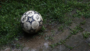 A Muddy Football Lays Unclaimed In The Grass. Wallpaper