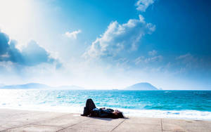 A Person Laying On A Bench Near The Ocean Wallpaper