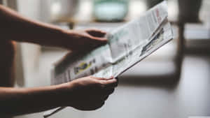 A Person Reading A Newspaper In Front Of A Window Wallpaper