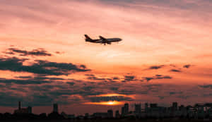 A Plane Flying Over A City At Sunset Wallpaper