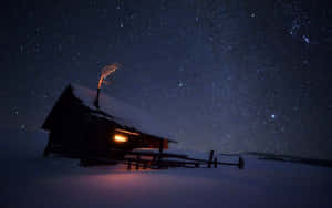 A Small Cabin Under The Stars In The Snow Wallpaper