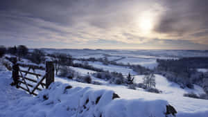 A Snow Covered Field With A Fence And Sun Wallpaper