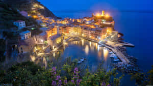 A Town Is Lit Up At Night On The Coast Wallpaper