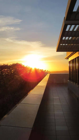 A View Of The Sun Setting Over A Rooftop Wallpaper